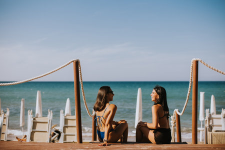 Two smiling young women in bikini sitting and enjoying vacation on the beachの写真素材