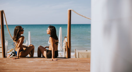 Two smiling young women in bikini sitting and enjoying vacation on the beachの写真素材