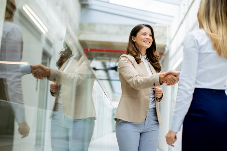 Two pretty young business women handshaking in the office hallwayの写真素材