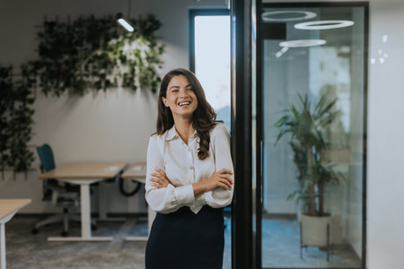 Pretty young business woman standing with arms crossed in the modern officeの写真素材