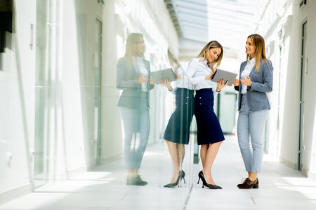 Two pretty young business women with digital tablet in the office hallwayの写真素材