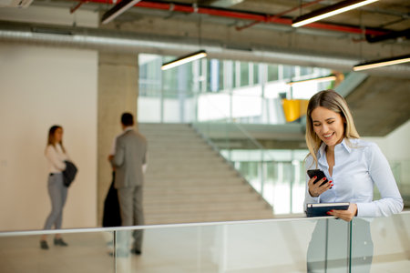Young business woman with notebook using mobile phone and standing in the modern office wallwayの写真素材