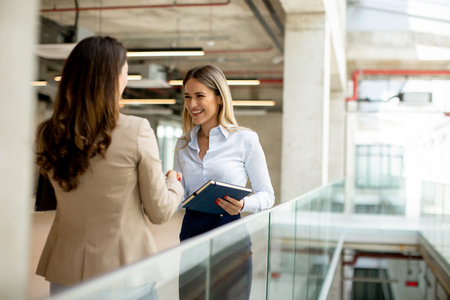 Two pretty young business women with paper notebook in the office hallwayの写真素材