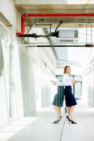 Young business woman with digital tablet standing in the modern office wallwayの写真素材