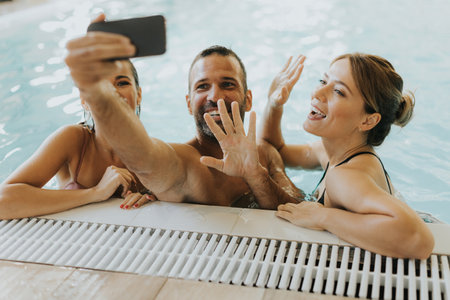 Handsome young people relaxing in the indoor swimming pool and taking selfie with mobile phoneの写真素材