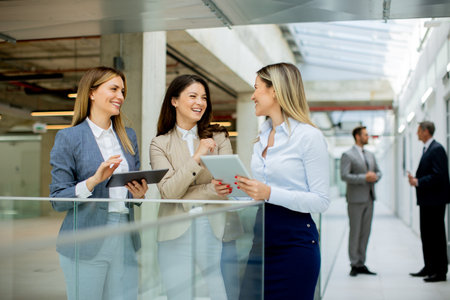 Three pretty young business women with digital tablets discussing business ideas in the office hallwayの写真素材