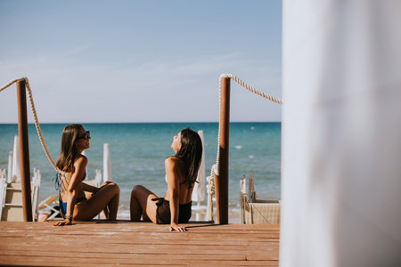 Two smiling young women in bikini sitting and enjoying vacation on the beachの写真素材