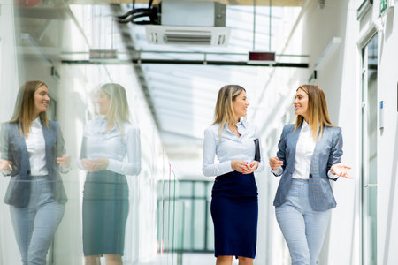 Two pretty young business women walking and discussing in the office hallwayの写真素材