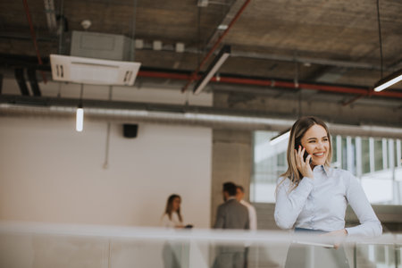 Young business woman with notebook using mobile phone and standing in the modern office wallwayの写真素材