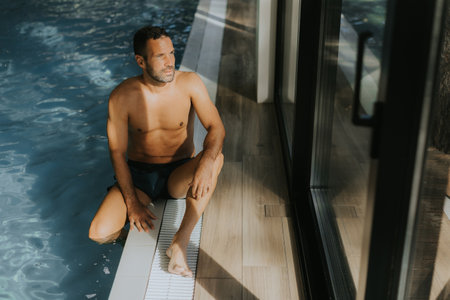 Handsome young man relaxing on the edge of a indoor swimming poolの写真素材