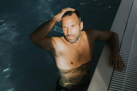 Handsome young man relaxing on the edge of a indoor swimming poolの写真素材