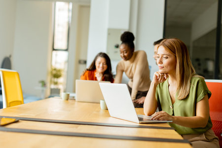 Pretty business woman working on laptop with her young multiethnic startup team working in the modern officeの写真素材