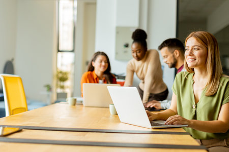 Pretty business woman working on laptop with her young multiethnic startup team working in the modern officeの写真素材