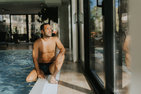 Handsome young man relaxing on the edge of a indoor swimming poolの写真素材