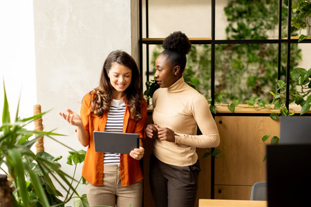 Two pretty young business women with digital tablet standing in the modern officeの写真素材