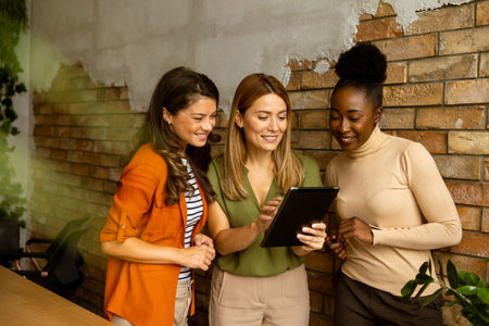 Three pretty young business women with digital tablet standing by the brick wall in the industrial style officeの写真素材