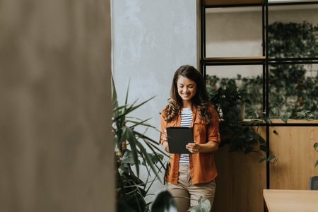 Pretty young woman standing with digital tablet at the officeの写真素材