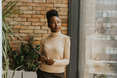 One pretty young African American business woman with digital tablet standing by the brick wall in the industrial style officeの写真素材