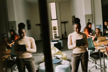 Young African American woman standing with digital tablet in front of her team at the modern officeの写真素材