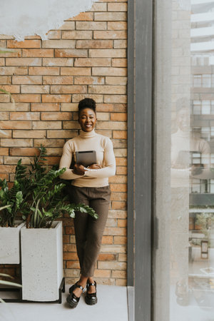 One pretty young African American business woman with digital tablet standing by the brick wall in the industrial style officeの写真素材