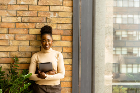 One pretty young African American business woman with digital tablet standing by the brick wall in the industrial style officeの写真素材