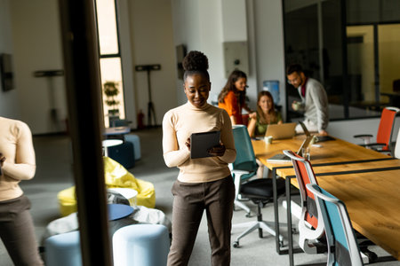 Young African American woman standing with digital tablet in front of her team at the modern office