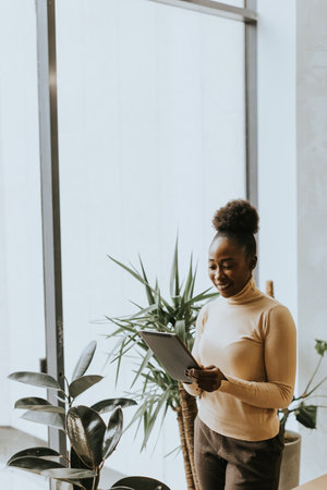 One pretty young African American business woman with digital tablet standing wall in the officeの写真素材