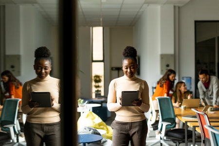 Young African American woman standing with digital tablet in front of her team at the modern officeの写真素材