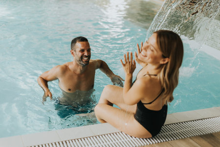 Handsome young couple having fun in the indoor swimming poolの写真素材