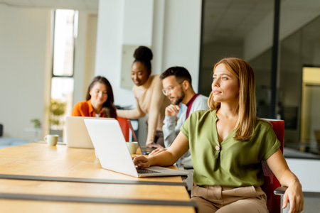 Pretty business woman working on laptop with her young multiethnic startup team working in the modern officeの写真素材