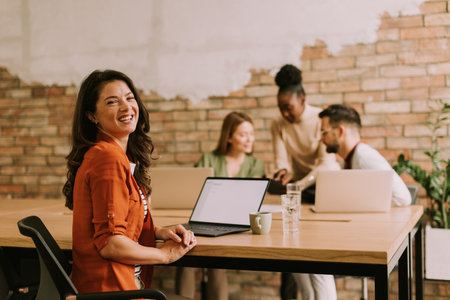 Pretty business woman working on laptop with her young multiethnic startup team in the modern officeの写真素材