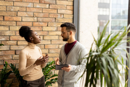 Handsome young multiethnic business couple with digital tablet standing and discussing in the modern officeの写真素材