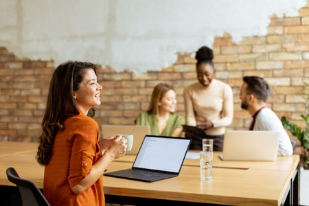 Pretty business woman working on laptop with her young multiethnic startup team working in the modern officeの写真素材