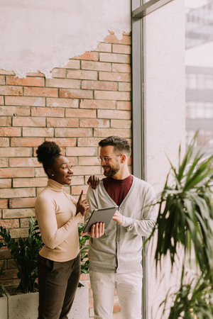 Handsome young multiethnic business couple with digital tablet standing and discussing in the industrial style officeの写真素材