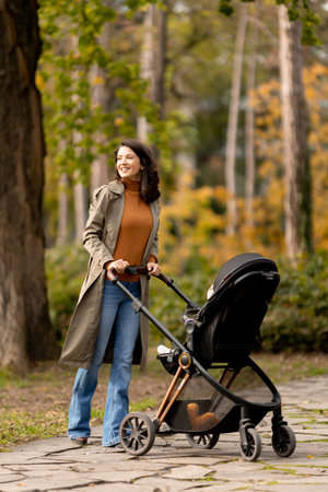 Young woman with a cute baby girl in baby stroller at the autumn parkの写真素材