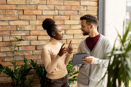 Handsome young multiethnic business couple with digital tablet standing and discussing in the modern officeの写真素材