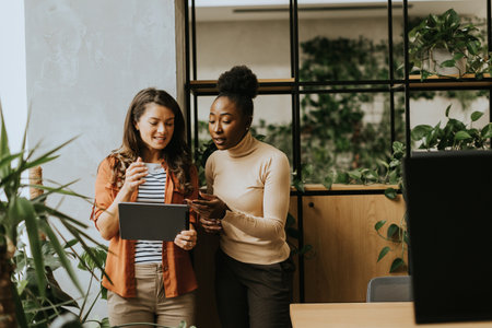 Two pretty young business women with digital tablet standing in the modern officeの写真素材
