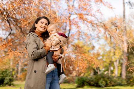 Young woman holding a cute baby girl in the autumn parkの写真素材