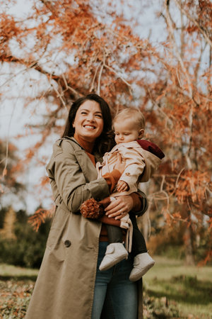 Young woman holding a cute baby girl in the autumn parkの写真素材