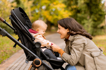 Young woman with a cute baby girl in baby stroller at the autumn parkの写真素材