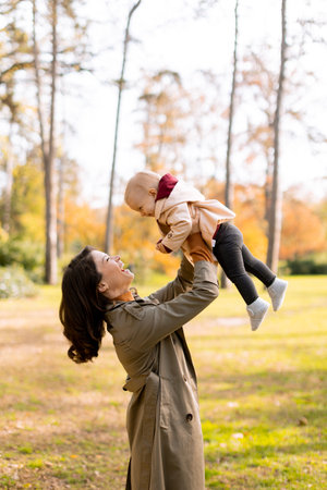 Young woman holding a cute baby girl in the autumn parkの写真素材