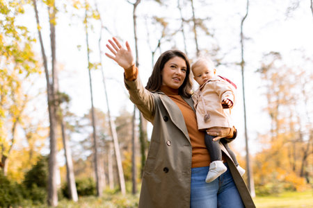 Young woman holding a cute baby girl in the autumn parkの写真素材