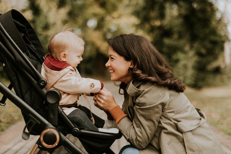 Young woman with a cute baby girl in baby stroller at the autumn parkの写真素材