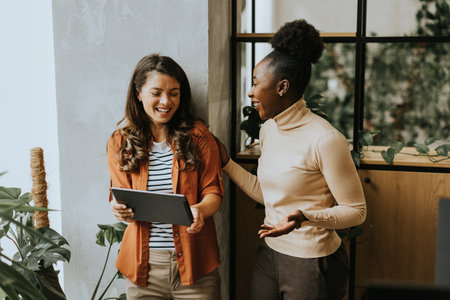 Two pretty young business women with digital tablet standing in the modern officeの写真素材