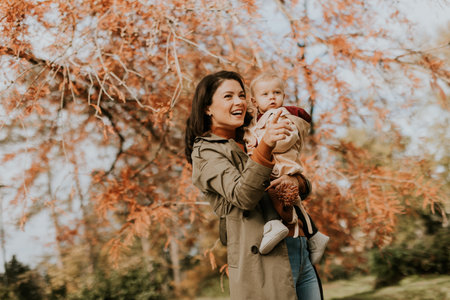Young woman holding a cute baby girl in the autumn parkの写真素材