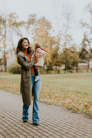 Young woman holding a cute baby girl in the autumn parkの写真素材