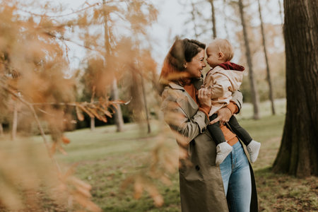 Young woman holding a cute baby girl in the autumn parkの写真素材