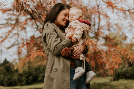 Young woman holding a cute baby girl in the autumn parkの写真素材