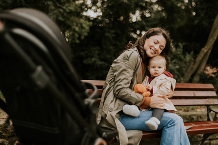 Young woman sitting on a bench with a cute baby girl in the autumn parkの写真素材