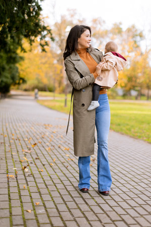 Young woman holding a cute baby girl in the autumn parkの写真素材